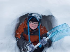 Gutt som titter ut av en snøhule.
