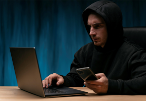 Mørkkledd skummel mann på PC og med mobilen. 